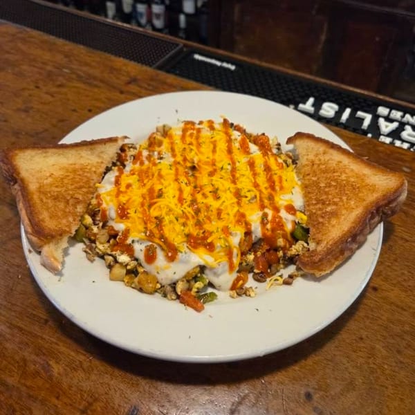 A breakfast skillet with gravy, cheese, and hot sauce, served with two pieces of toast.