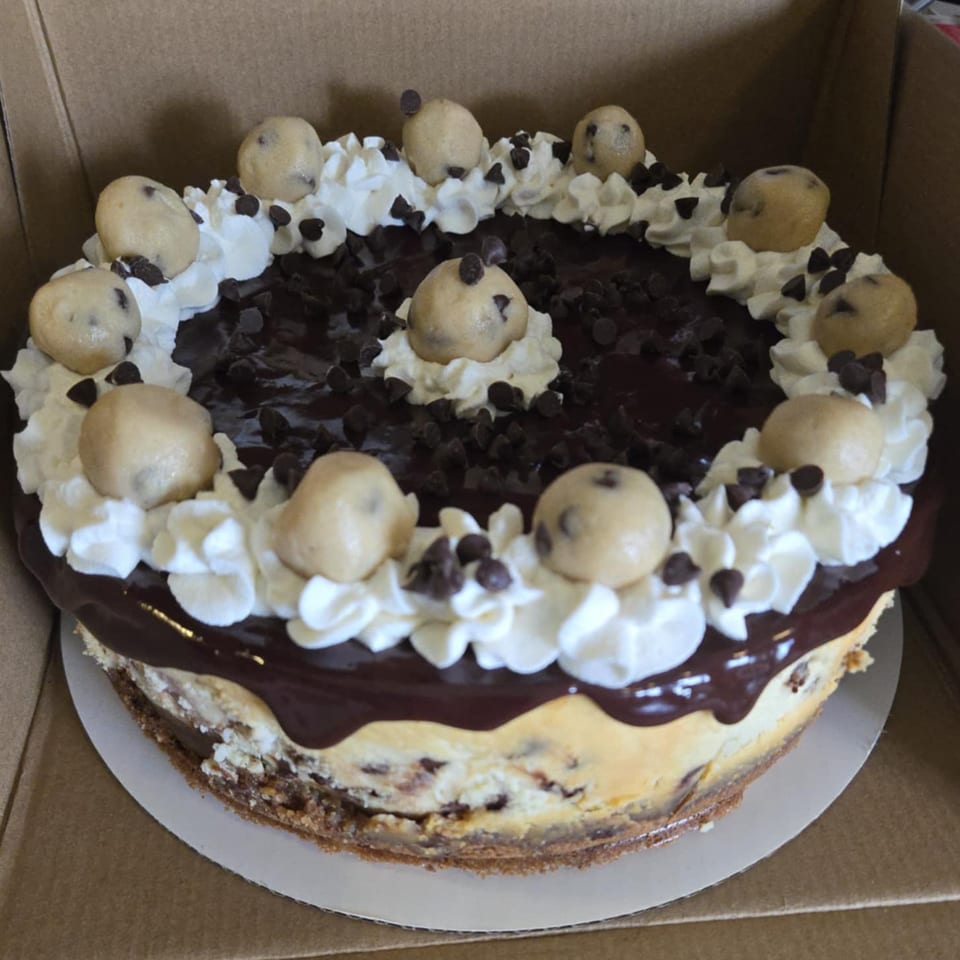 A cheesecake with chocolate ganache, whipped cream, chocolate chips, and cookie dough balls.