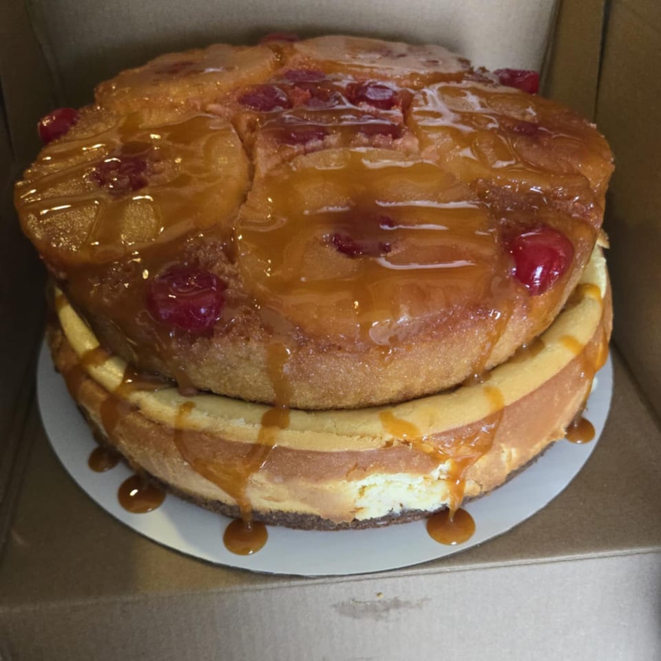A two-tiered dessert with a pineapple upside-down cake on top of a cheesecake, drizzled with caramel.